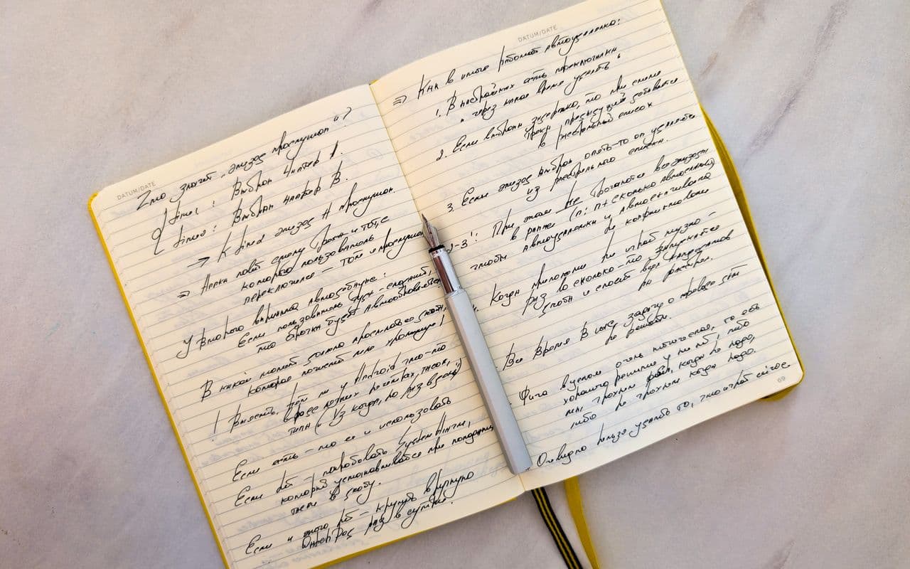 An open notebook filled edge to edge with handwriting, a fountain pen laid across both pages.