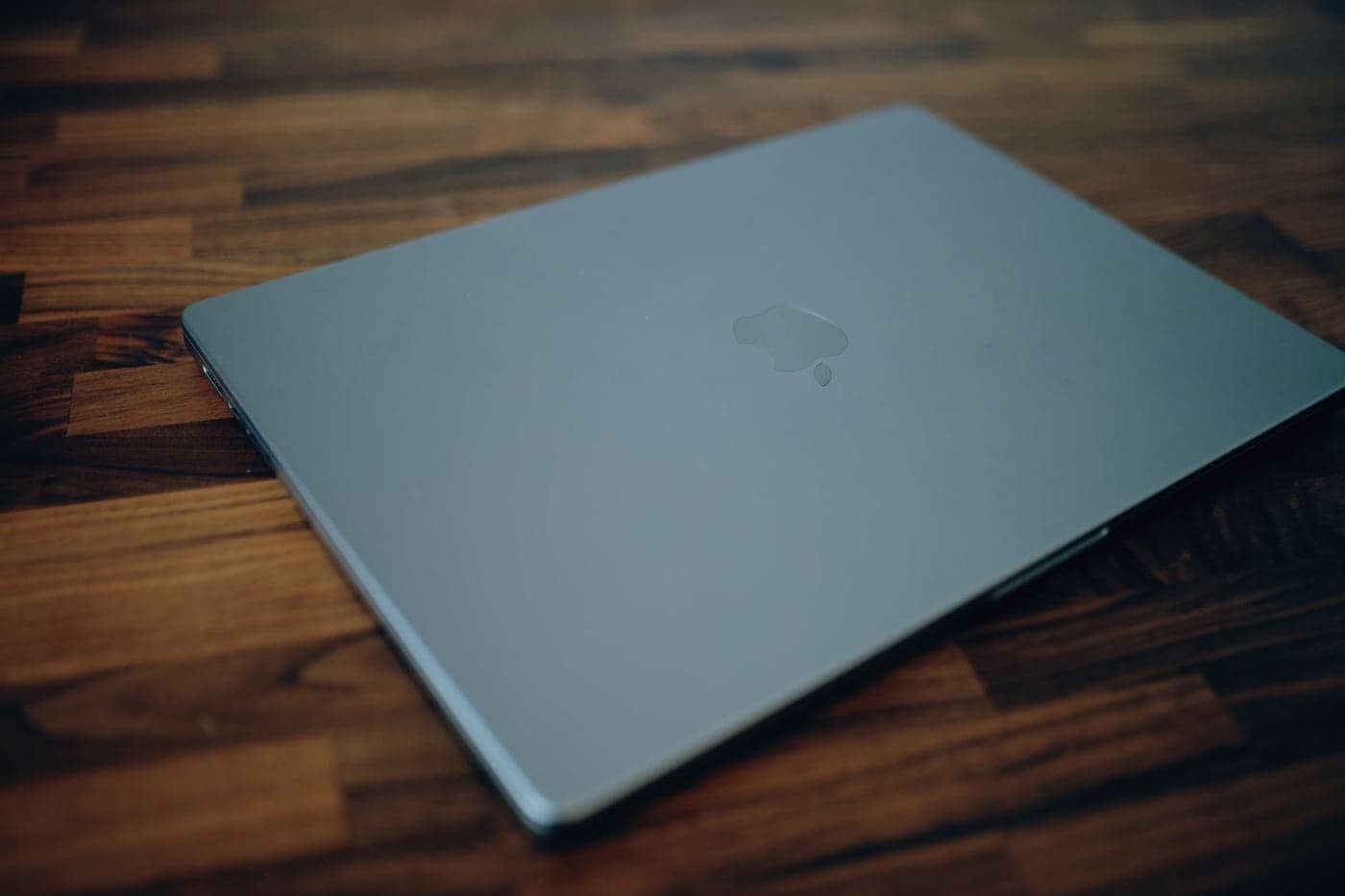 A closed space grey MacBook lying on a dark wooden table.