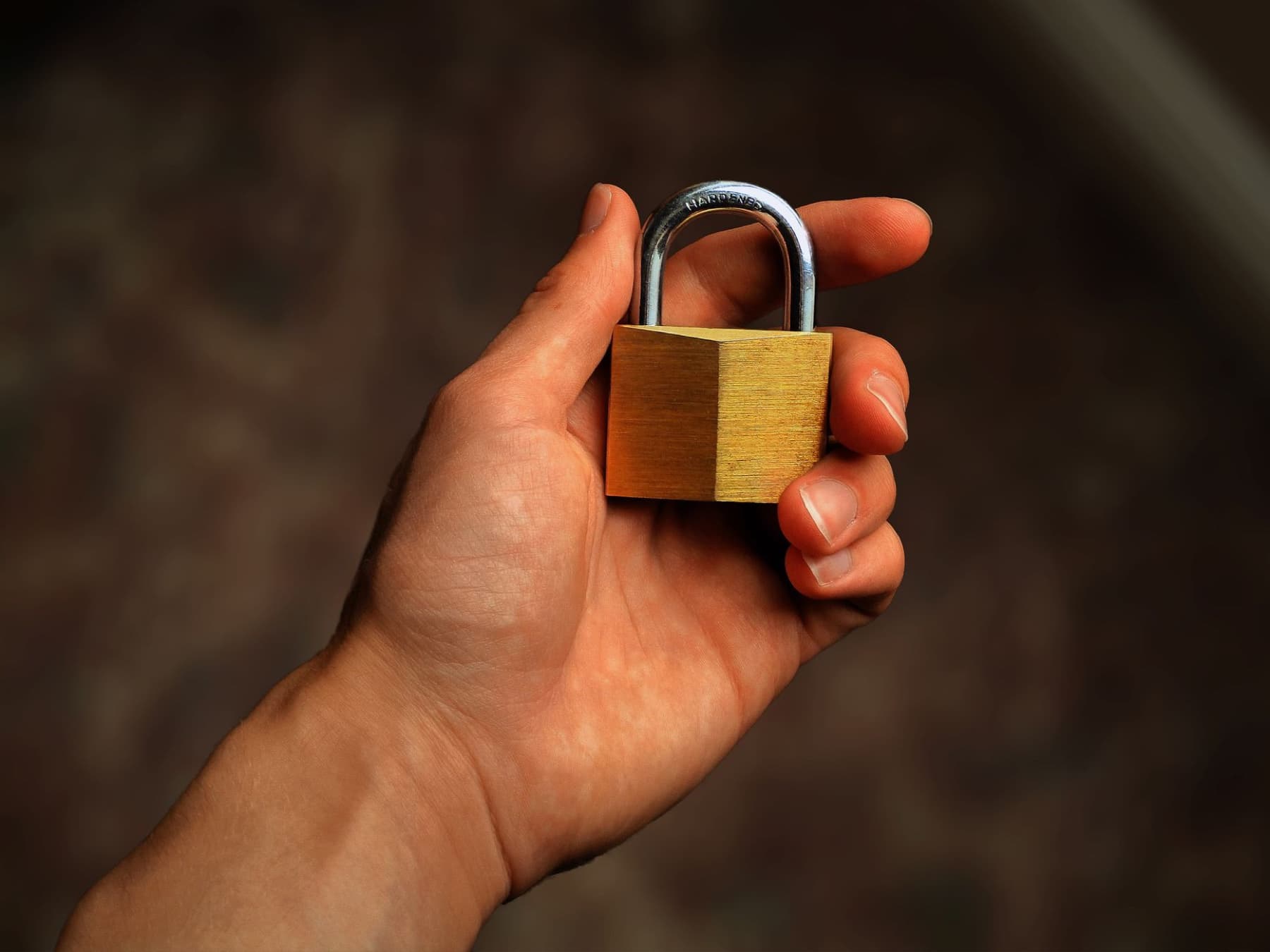 A hand holding a small brass padlock against a dark background.